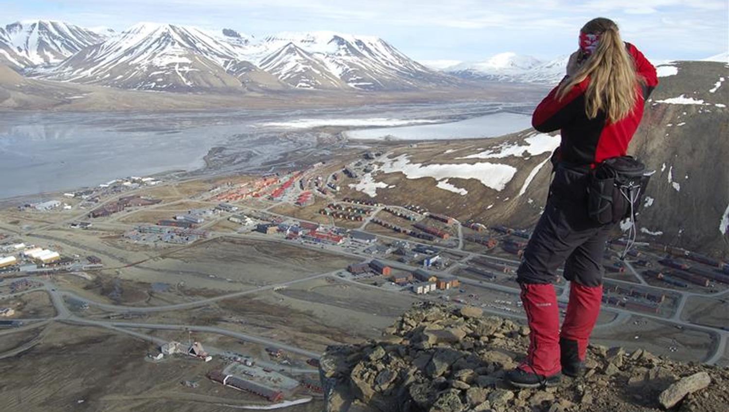 A person standing on top of Platåfjellet looking down on the buildings in Longyearbyen in the background