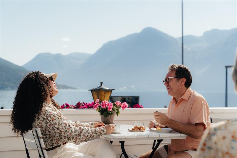 Guests with coffee and croissants on the terrace at Utne Hotel, with the Hardangerfjord and mountains behind.