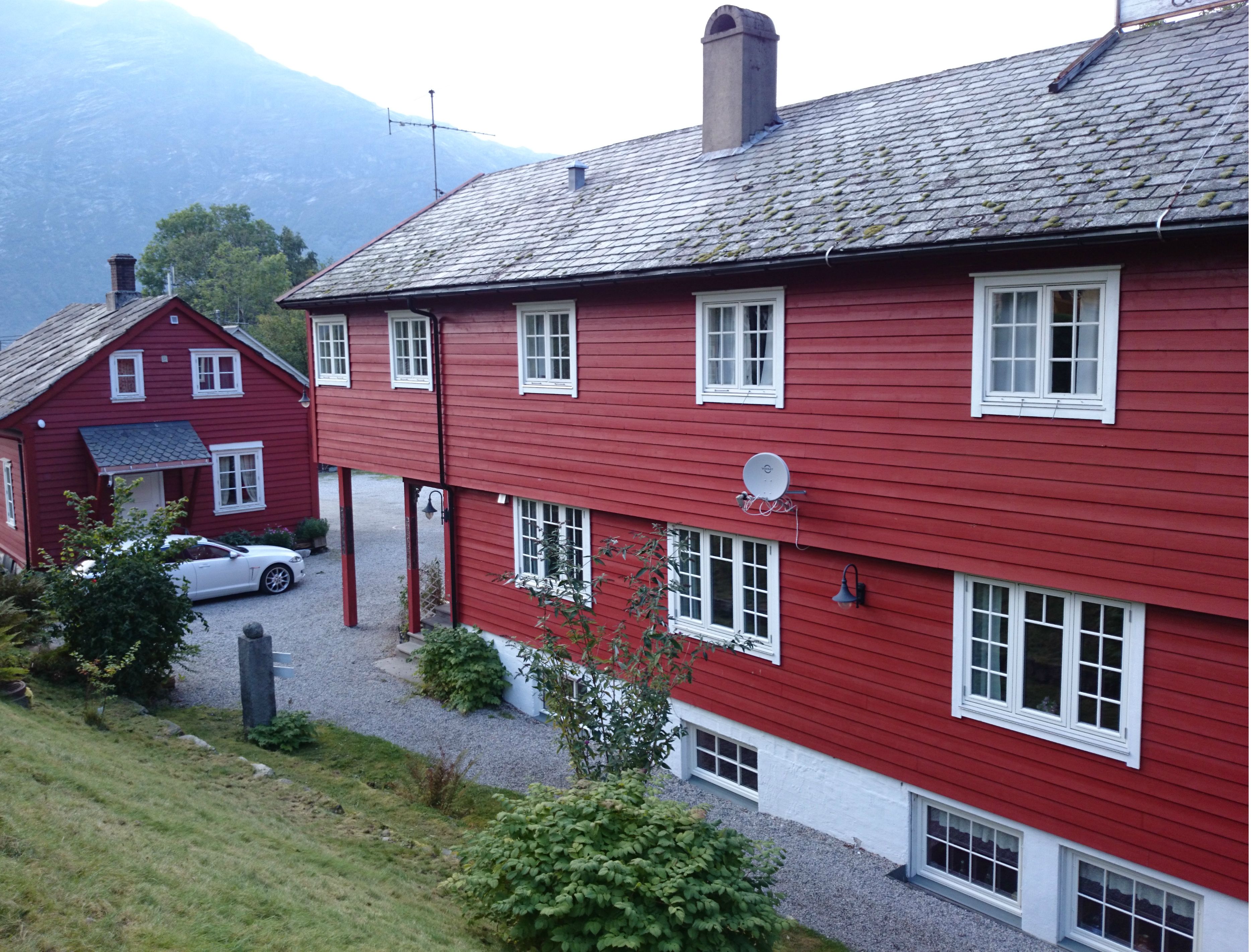 Red-painted main buildings at Ullensvang Gjesteheim, surrounded by mountains, orchards and classic West Norwegian charm.