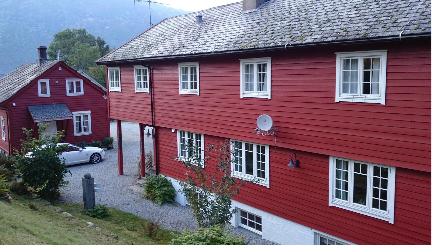 Red-painted main buildings at Ullensvang Gjesteheim, surrounded by mountains, orchards and classic West Norwegian charm.