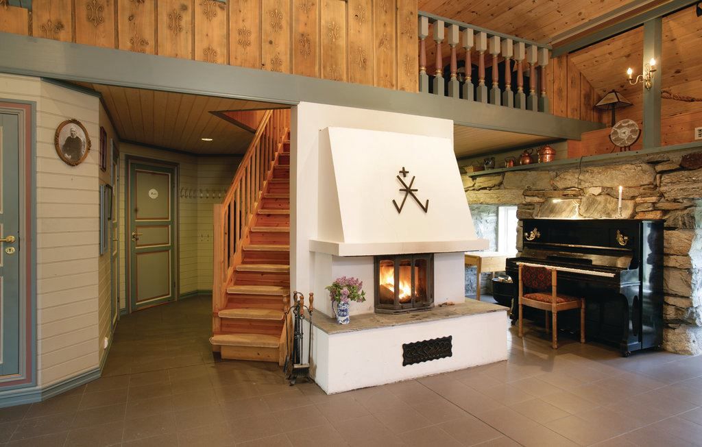 Orheimstunet in Nordfjord - Rustic cabin interior with a central white fireplace, wooden stairs to a loft, stone wall, and a black piano..