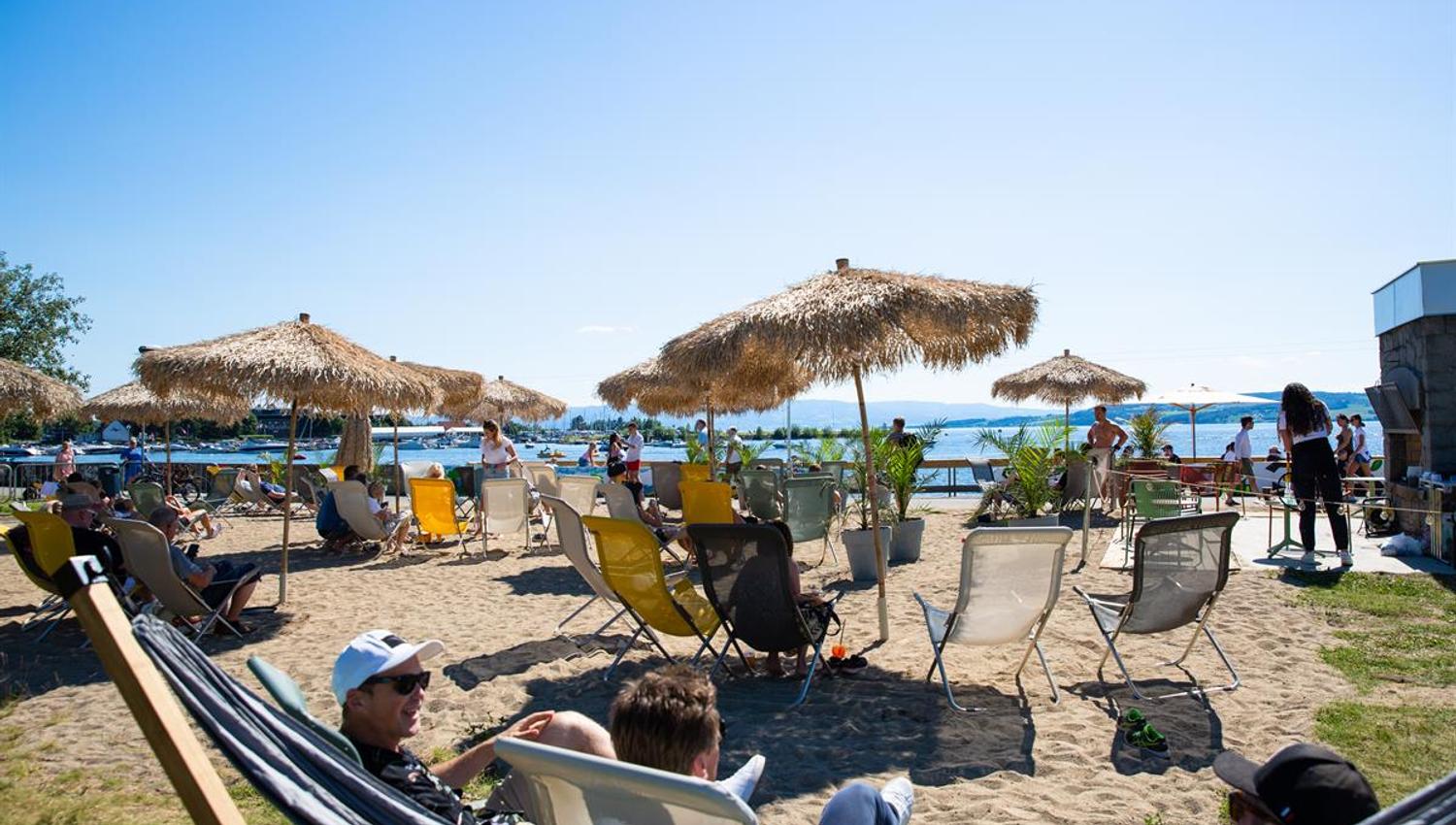 Solfylt strandområde med solsenger, parasoller og gjester som slapper av.