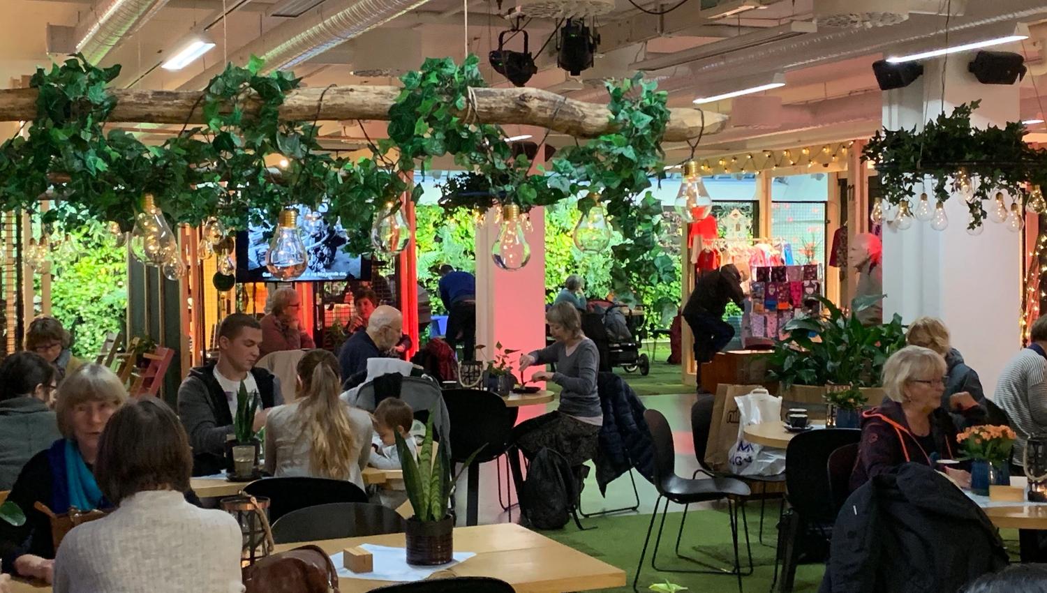 Folk i samtale og måltid på en koselig kafé med planter og dekorasjoner