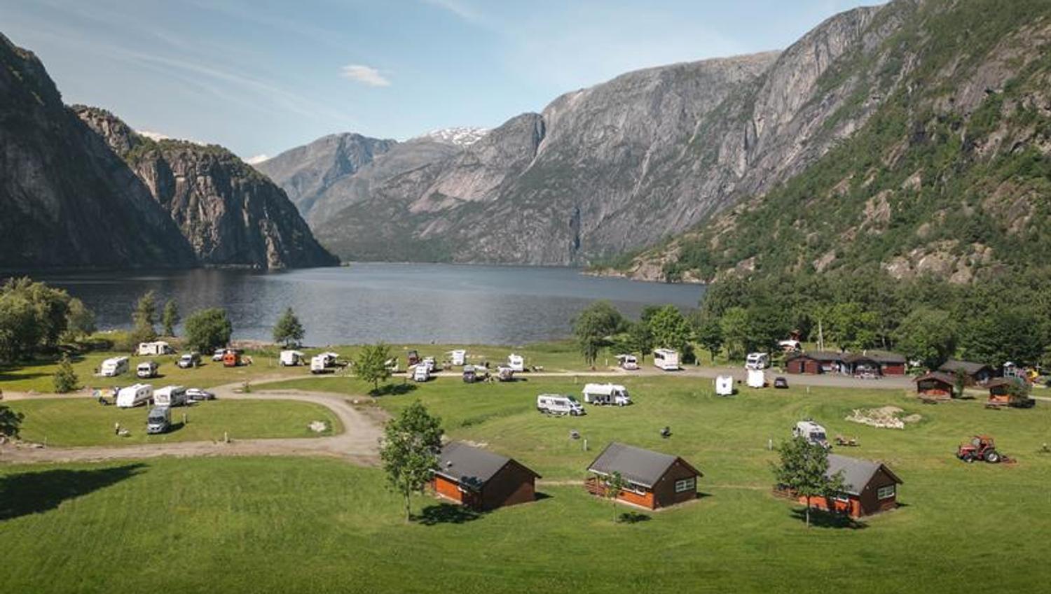 Sæbø camping sett fra hovedveien, med vann og fjell i bakgrunnen.