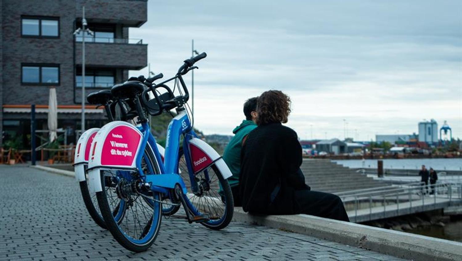 To personer som sitter på en bryggekant, med to bysykler bak dem