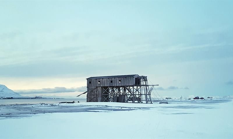 an old building in the foreground, with mountains and fjord in the background.