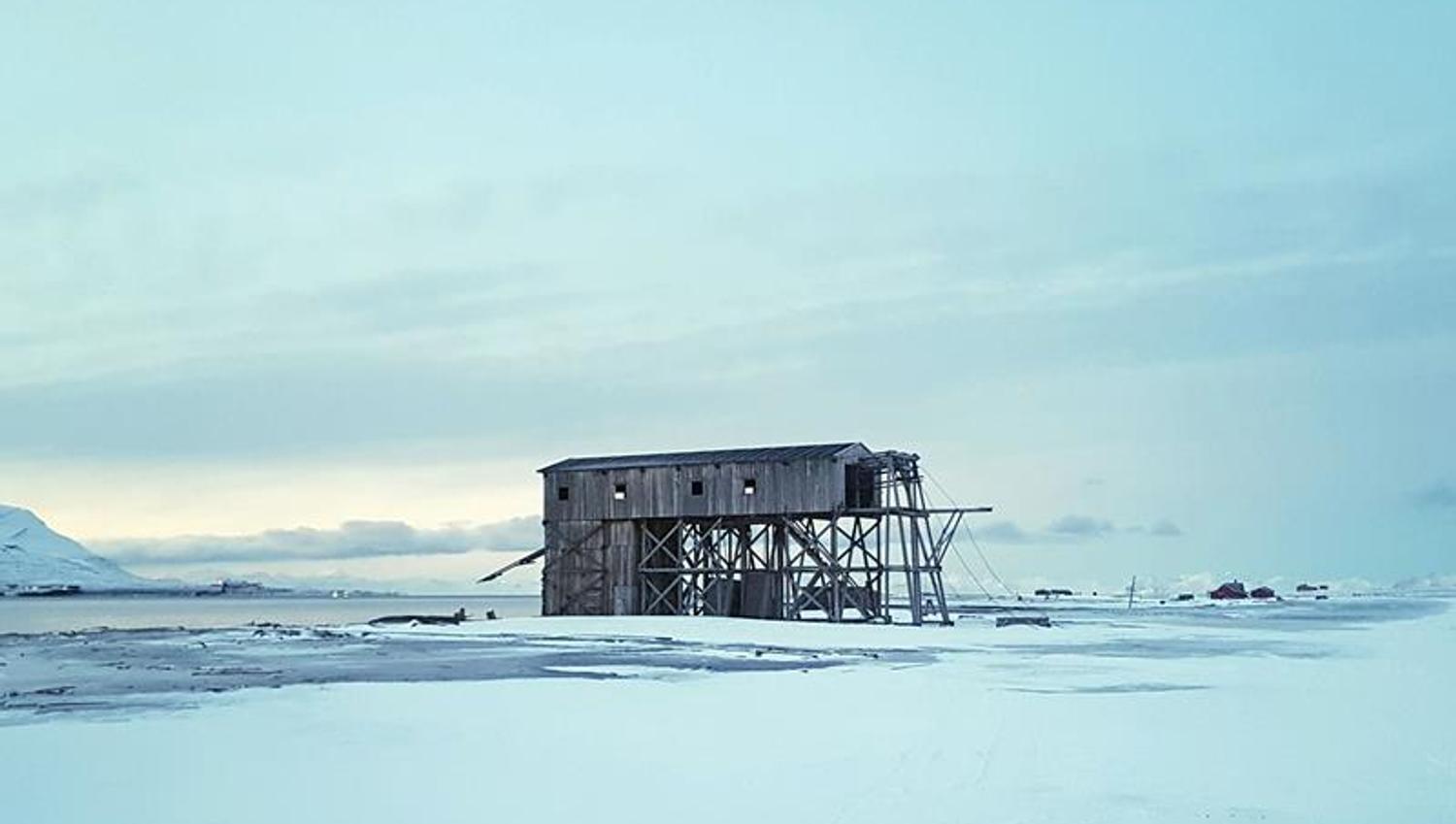an old building in the foreground, with mountains and fjord in the background.