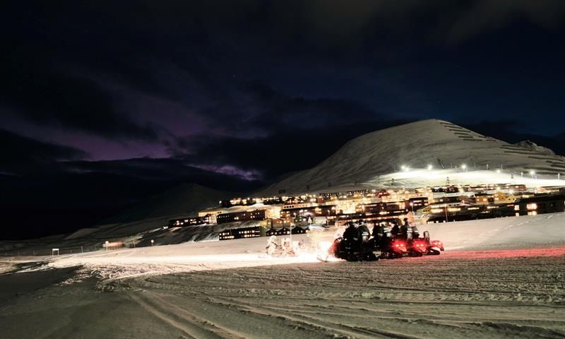 Snøscootere står på med Longyearbyen i bakgrunnen