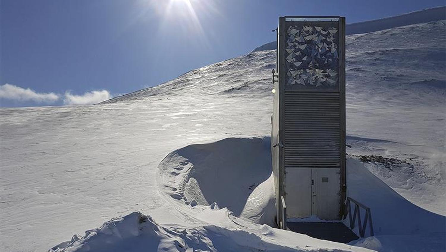 Inngangspartiet til Svalbard Globale Frøhvelv i lyse snødekte omgivelser med solskinn og blå himmel i bakgrunnen