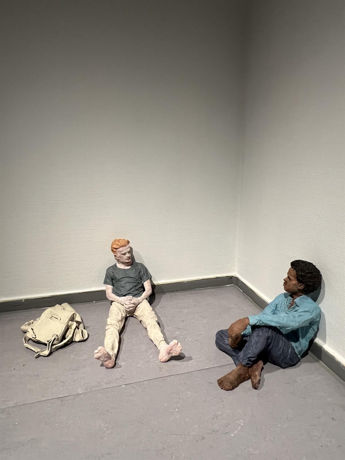 Two sculptural figures sitting on the floor near a wall with objects placed around.