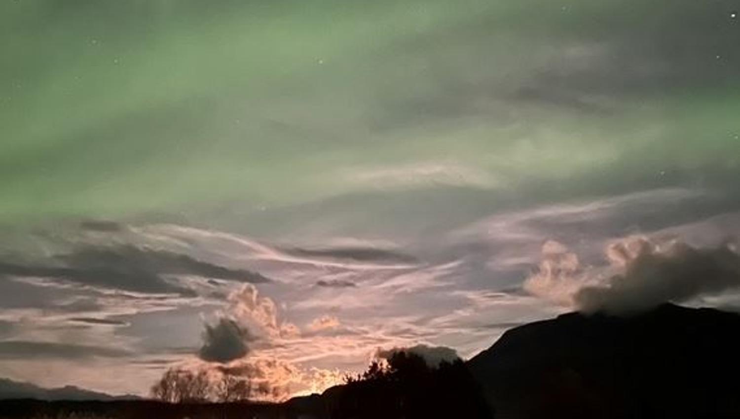 Northern Lights above the mountains and thin, contrasting clouds