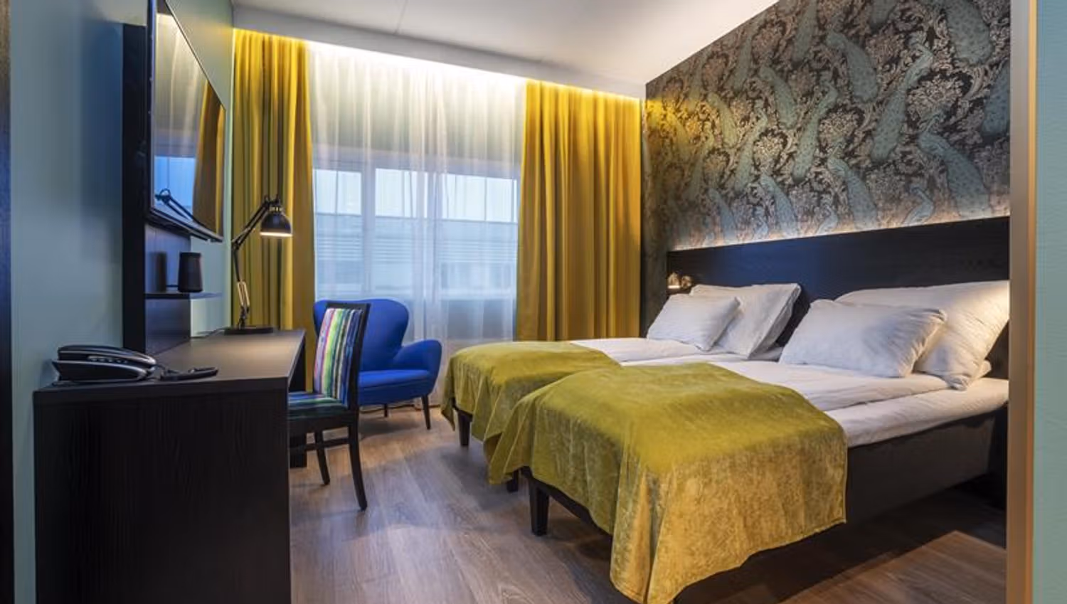 hotell rom med ddobbeltseng med gult sengeteppe og en blå stol