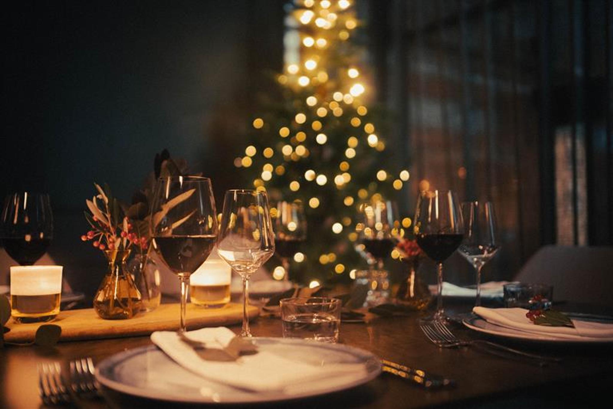 Table set for dining with wine glasses and a Christmas tree in the background