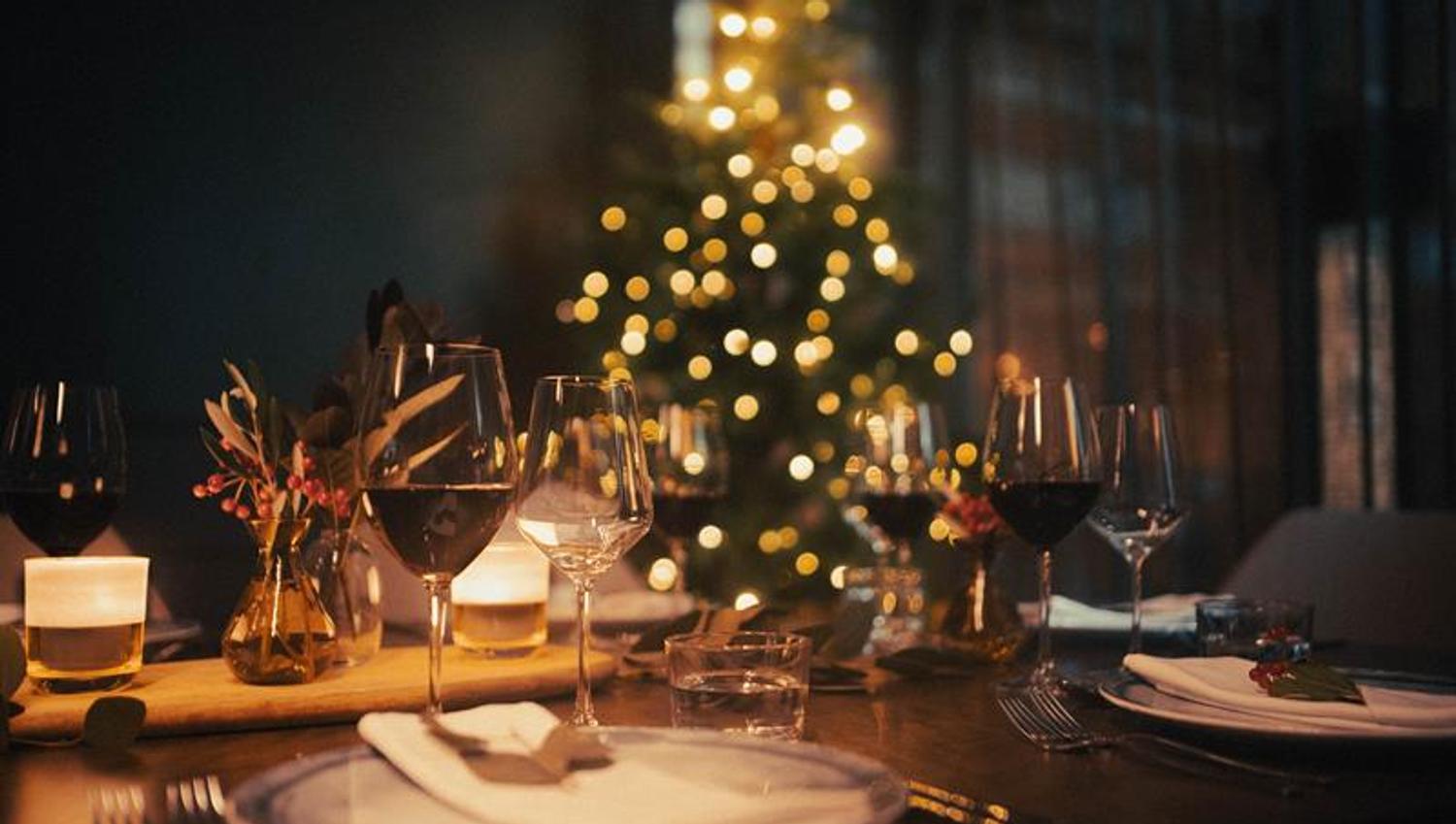 Table set for dining with wine glasses and a Christmas tree in the background