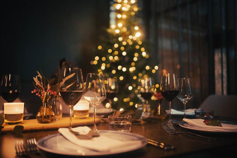 Table set for dining with wine glasses and a Christmas tree in the background