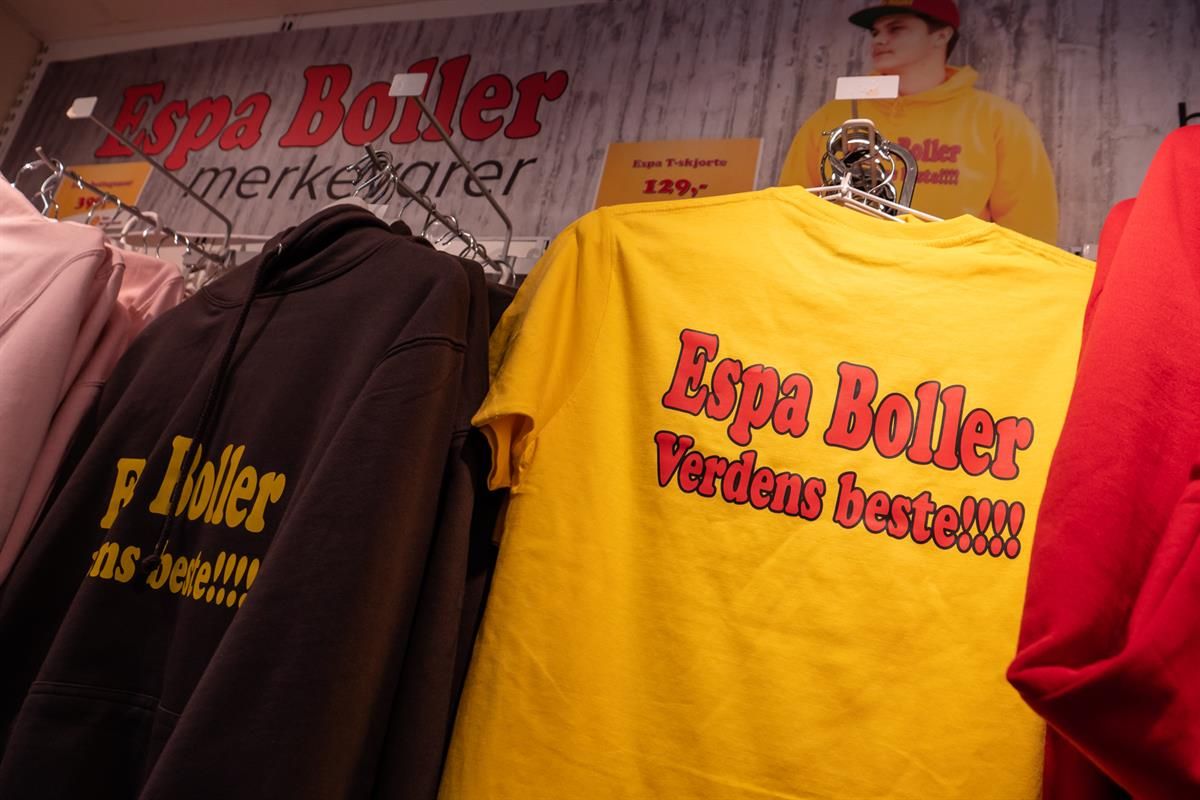 A yellow T-shirt with printed text hanging on a clothing rack in a store, surrounded by other garments and promotional items.
