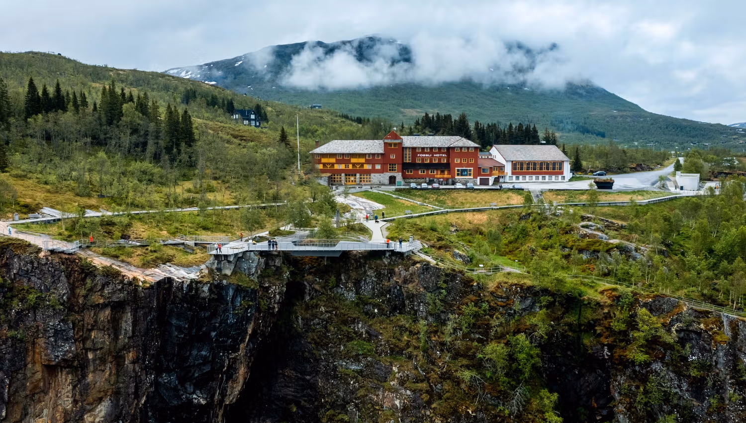 A drone shot of the Fossli Hotel sitting above the waterfall.