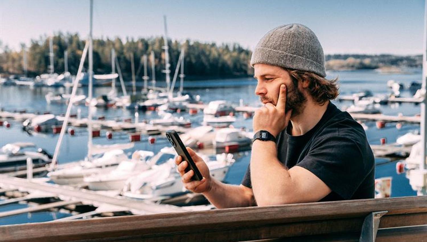 Man sitting with his mobile phone up by a harbour