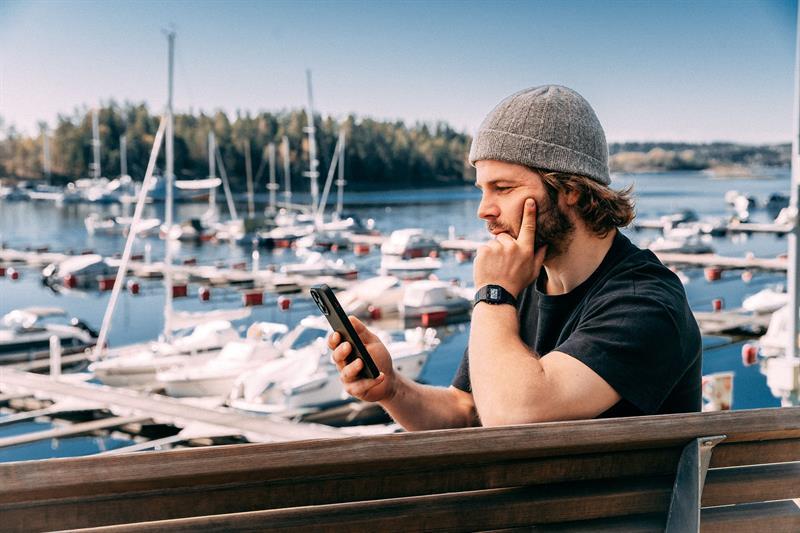 Man sitting with his mobile phone up by a harbour