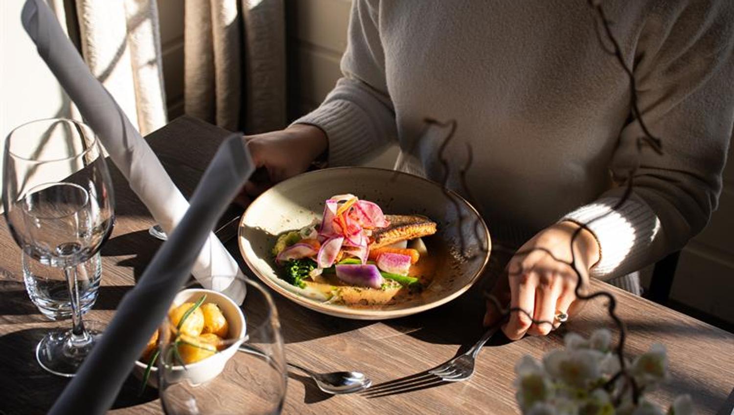 Lady at the table. Meat dish on plate. Sun through the window.