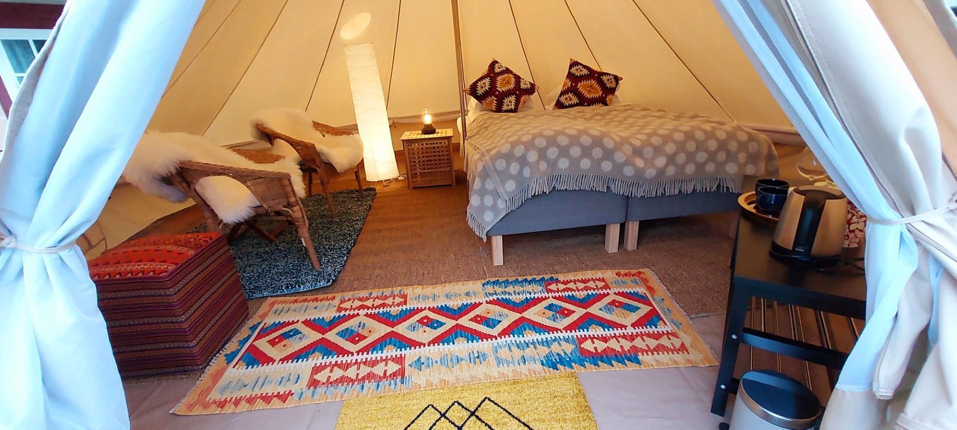 Interior of a glamping tent with a bed, rugs, and a small seating area, decorated with warm colors and textiles.