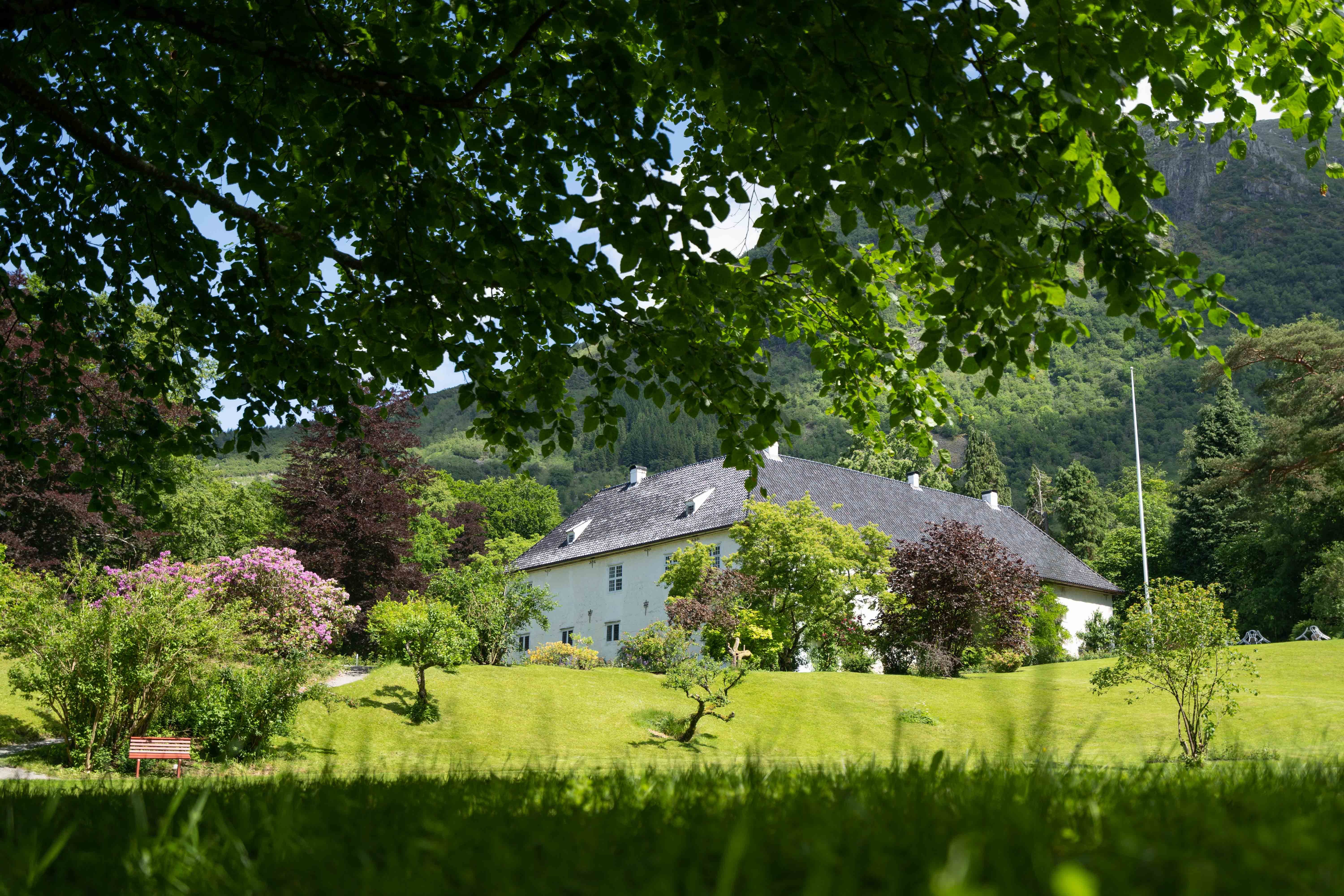 Historic property at Baroniet in Rosendal seen from a lush green garden with mountains in the background.