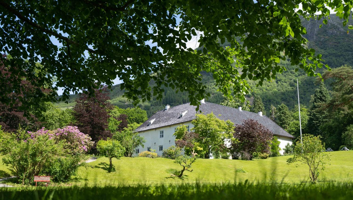 Historic property at Baroniet in Rosendal seen from a lush green garden with mountains in the background.