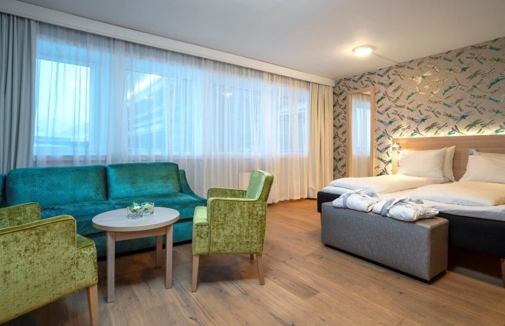Hotel room with two single beds, green seating furniture, and bird-patterned wallpaper.