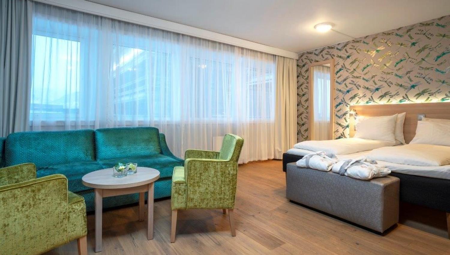 Hotel room with two single beds, green seating furniture, and bird-patterned wallpaper.