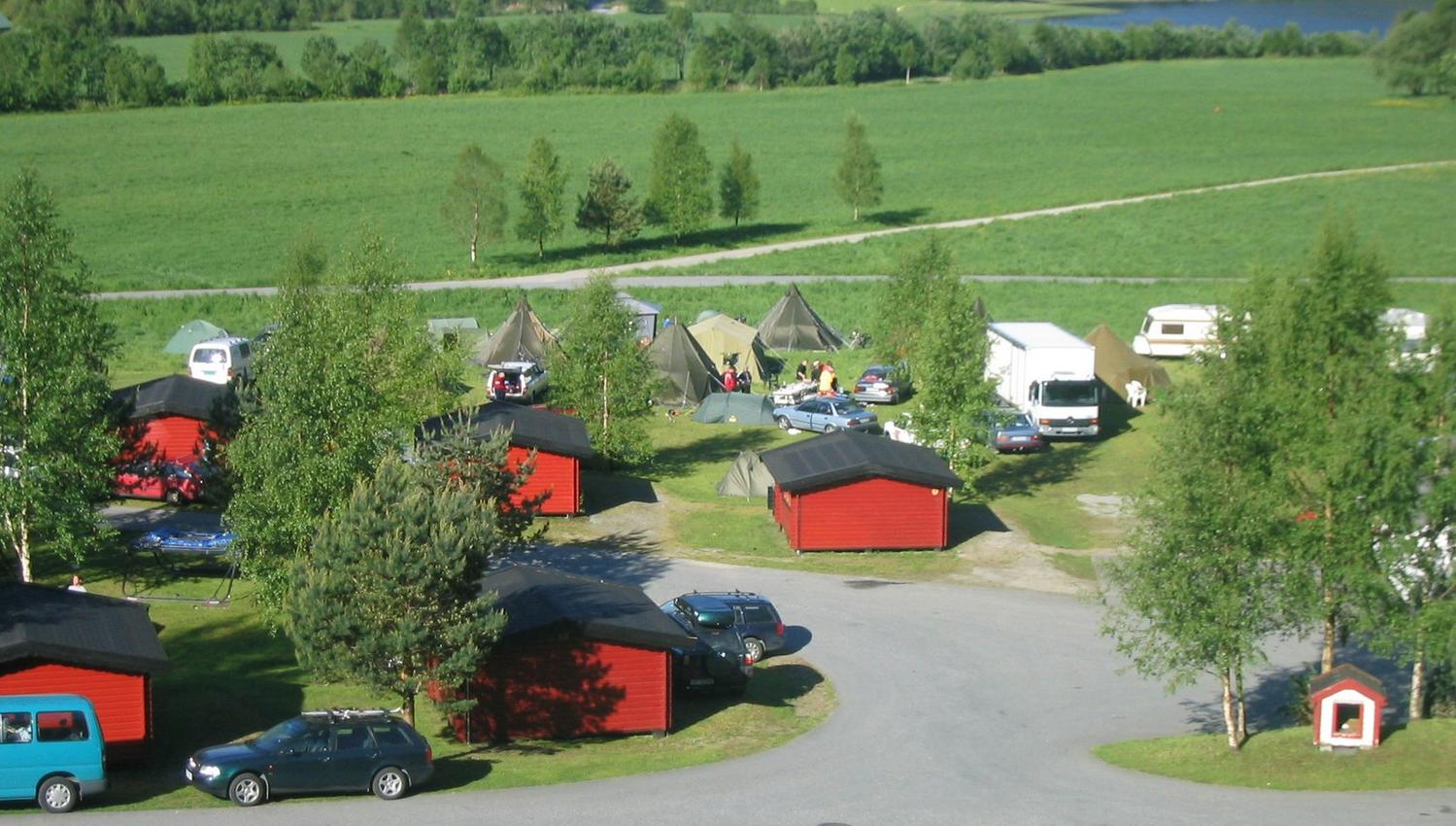The campsite at Folgefonn Cabins and Farm Camping surrounded by nature, tents, and cabins overlooking the water.