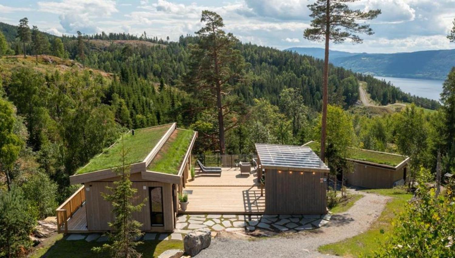Wooden cabin buildings surrounded by forest, overlooking mountains and a lake.