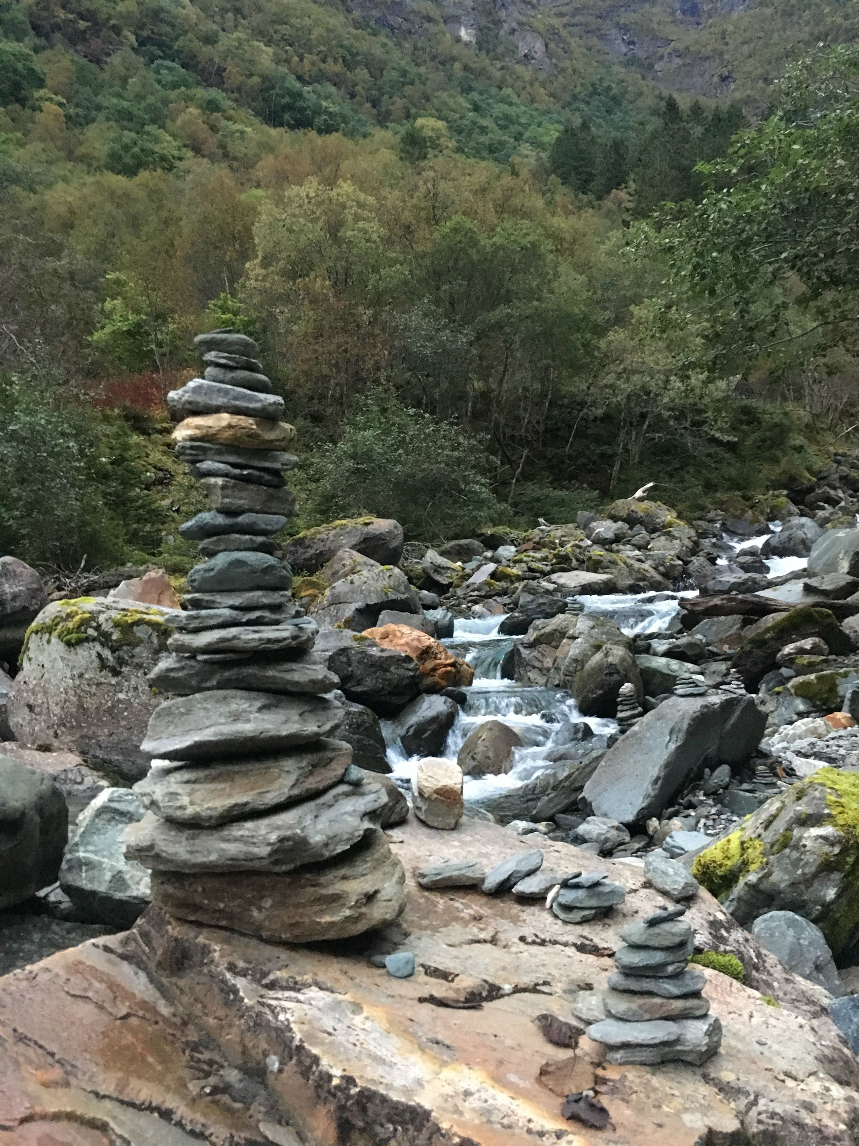 Stone cairns by the river in Elvedalen, surrounded by moss and mountain forest.

