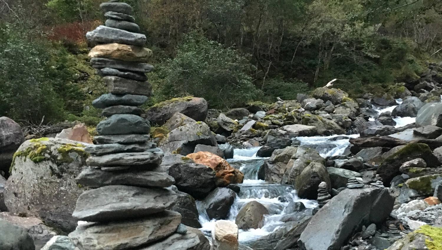 Stone cairns by the river in Elvedalen, surrounded by moss and mountain forest.