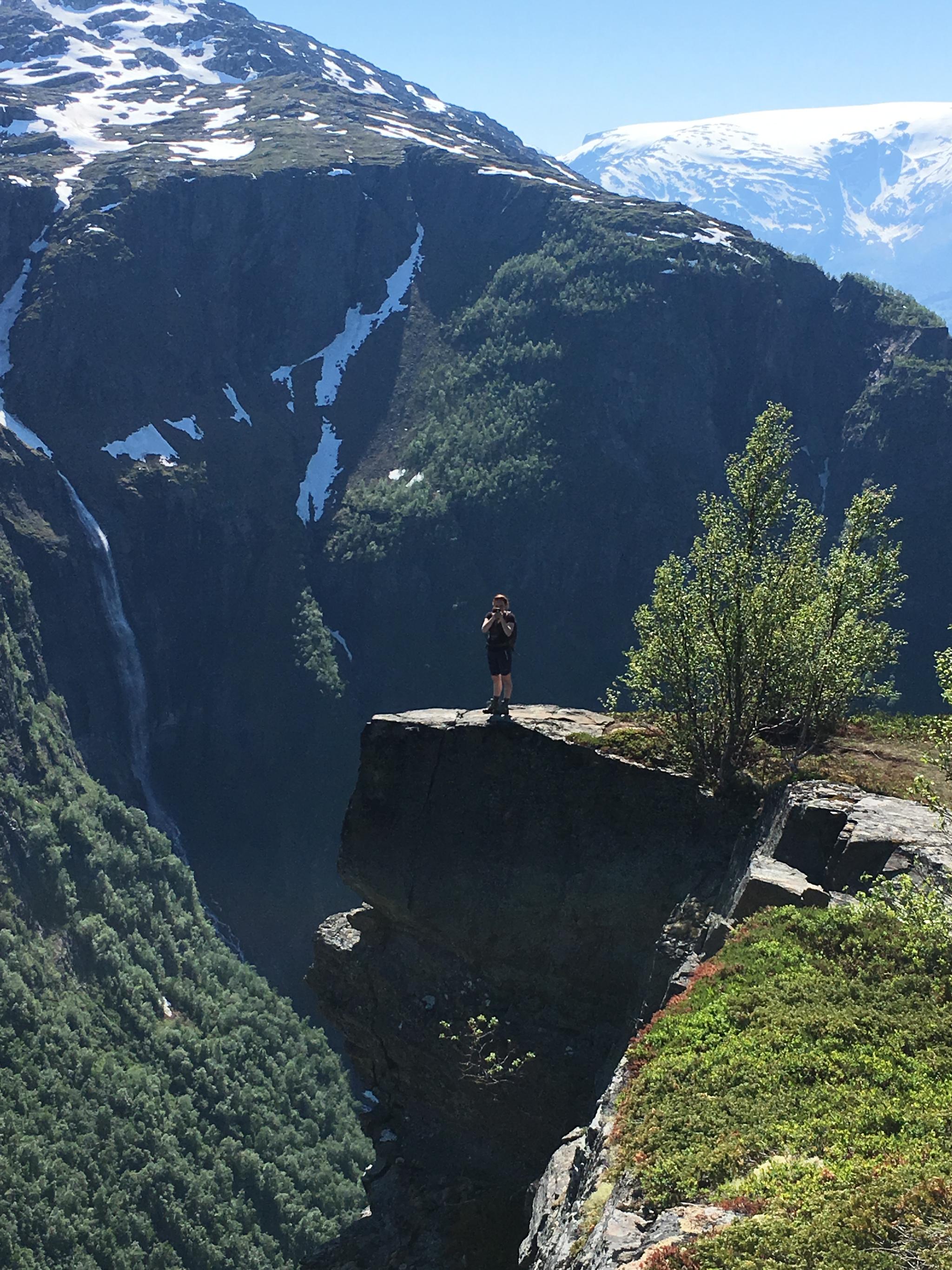 Person standing on a mountain ledge overlooking steep cliffs and a waterfall in Hardanger.
