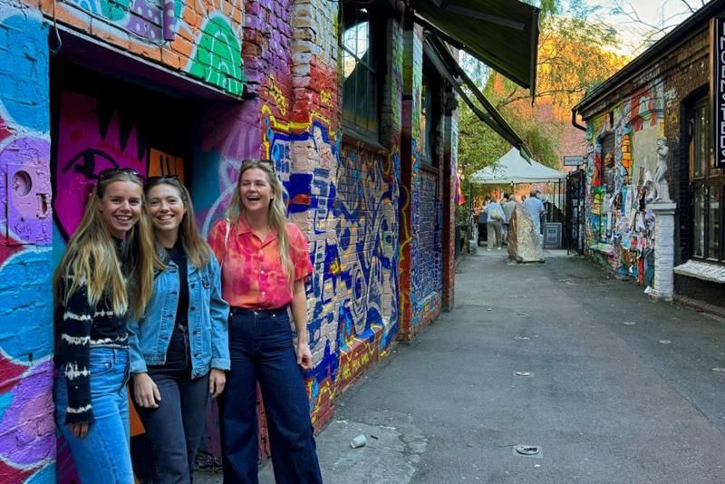 Three girls standing in front of a wall with graffiti on it