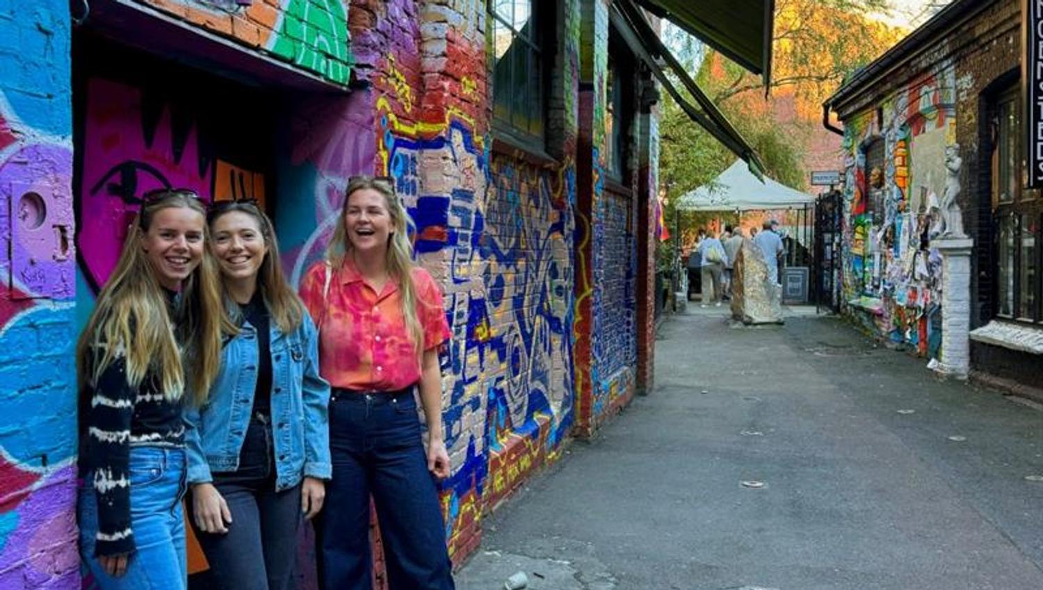 Three girls standing in front of a wall with graffiti on it