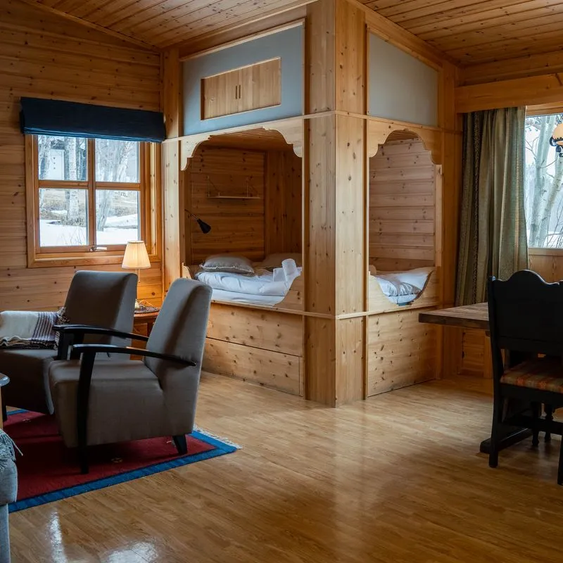 Cozy wooden cabin interior with twin beds, light, and seating area.