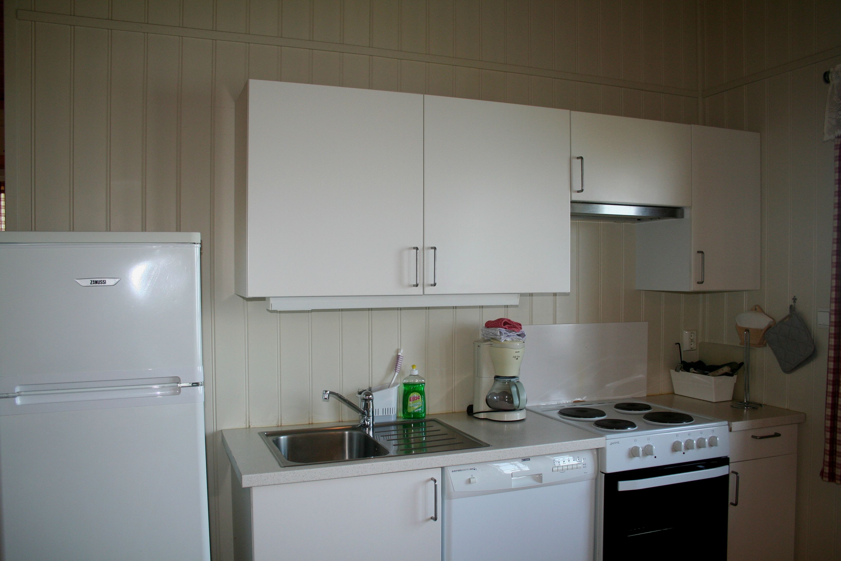 Modern kitchen area in a cabin at Oddland Camping with stove, fridge, and coffee maker.