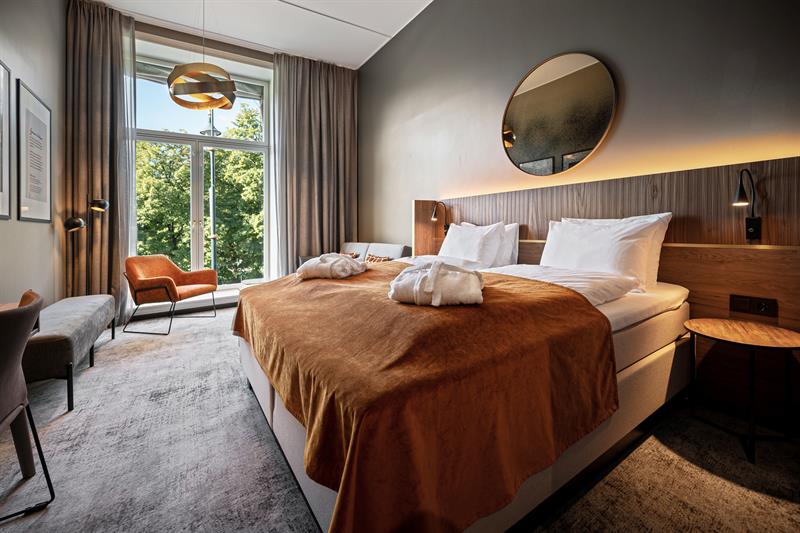Room interior of deluxe room with a large double bed and a large window.