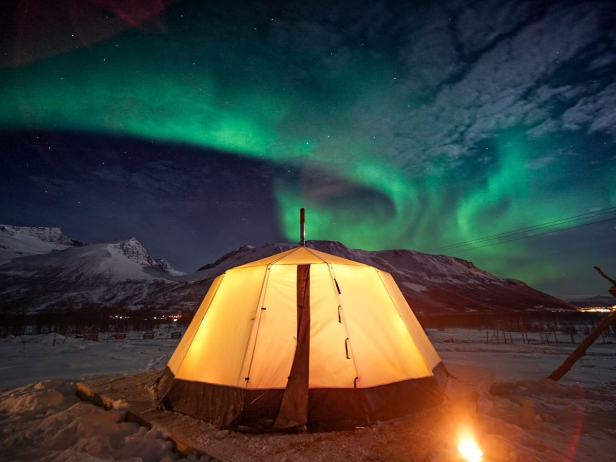 Illuminated lavvu beneath the Northern Lights at Tromsø Lapland’s Sámi camp near Tromsø.
