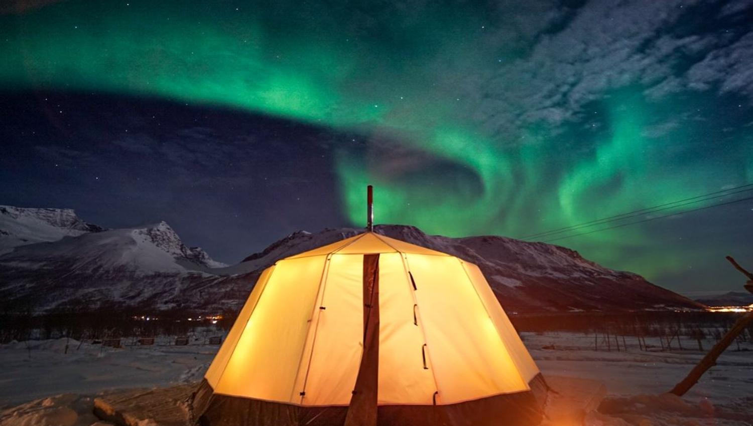 Illuminated lavvu beneath the Northern Lights at Tromsø Lapland’s Sámi camp near Tromsø.