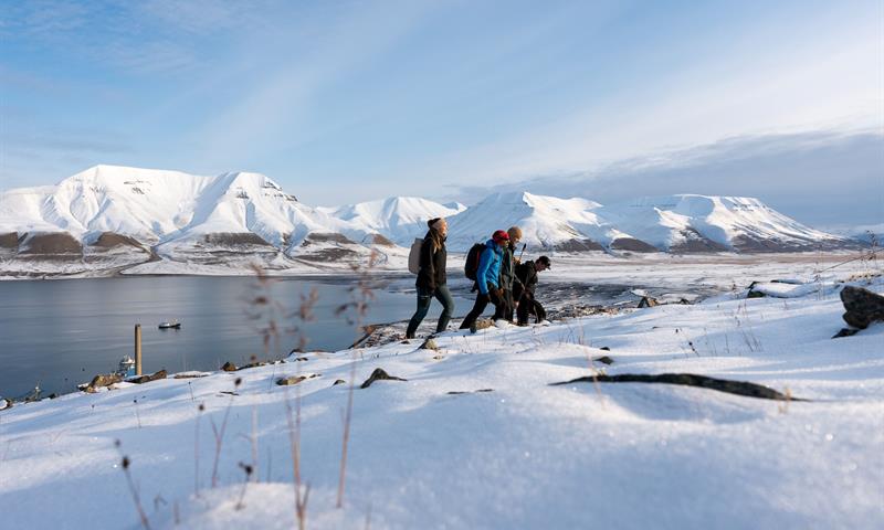 flere personer vandrer oppover fjellet i snødekt landskap
