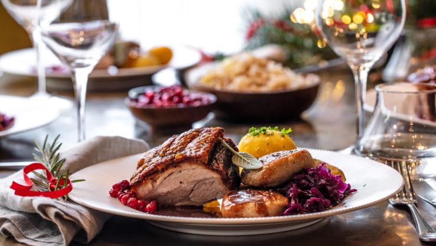 Bildet viser et pent dekket bord med en tallerken mat. På tallerkenen ligger det ribbe, poteter, saus og rødkål. Det står vinglass og pynt med lys rundt, så det ser ut som et koselig julemåltid.