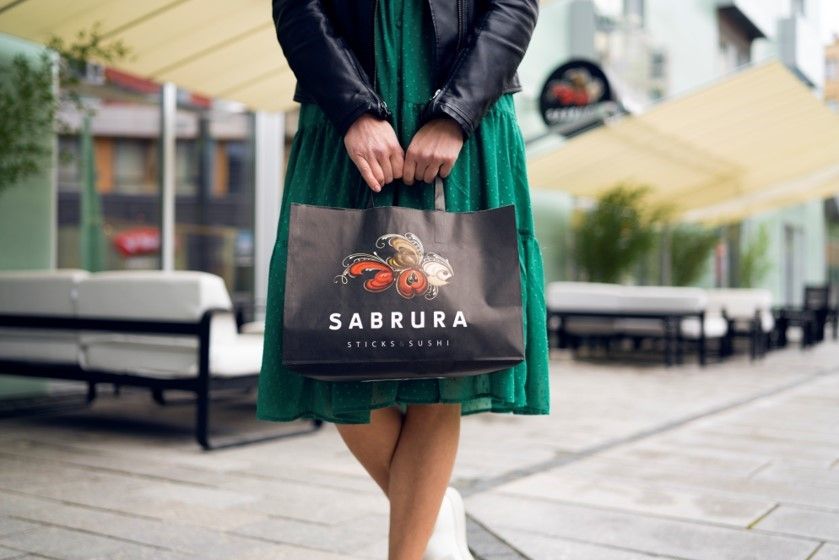 Person i grønn kjole som holder en papirpose med Sabrura logoen