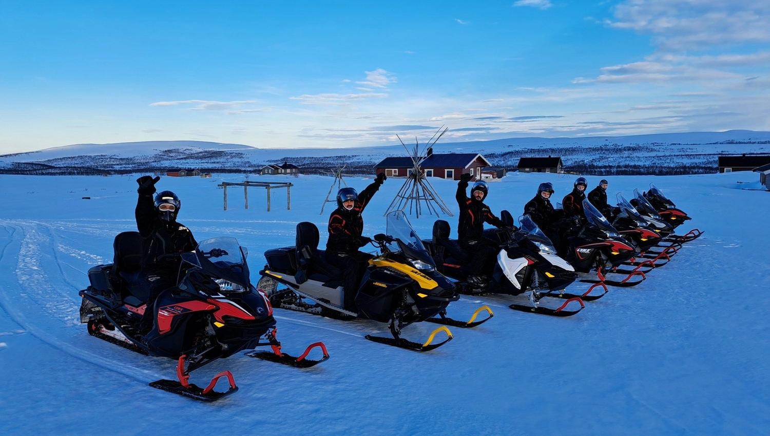 Groupe de personnes sur des motoneiges dans un paysage enneigé sous un ciel bleu.