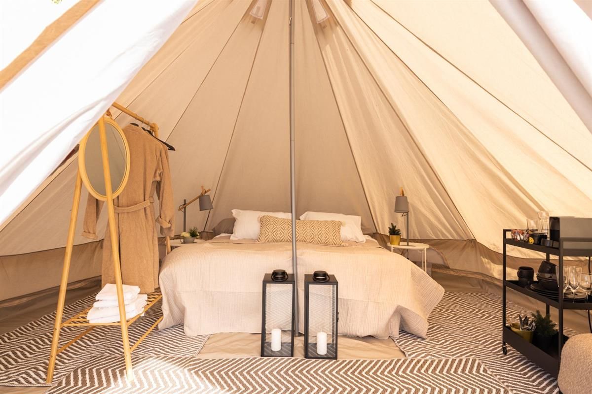  Interior of a glamping tent with a bed, rugs, and lanterns.