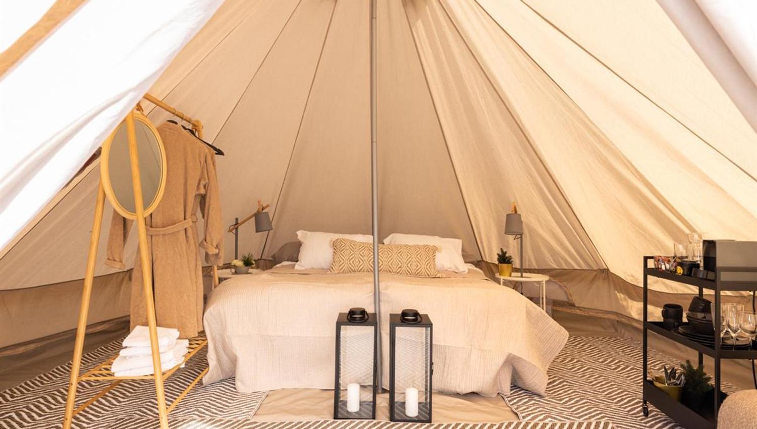 Interior of a glamping tent with a bed, rugs, and lanterns.