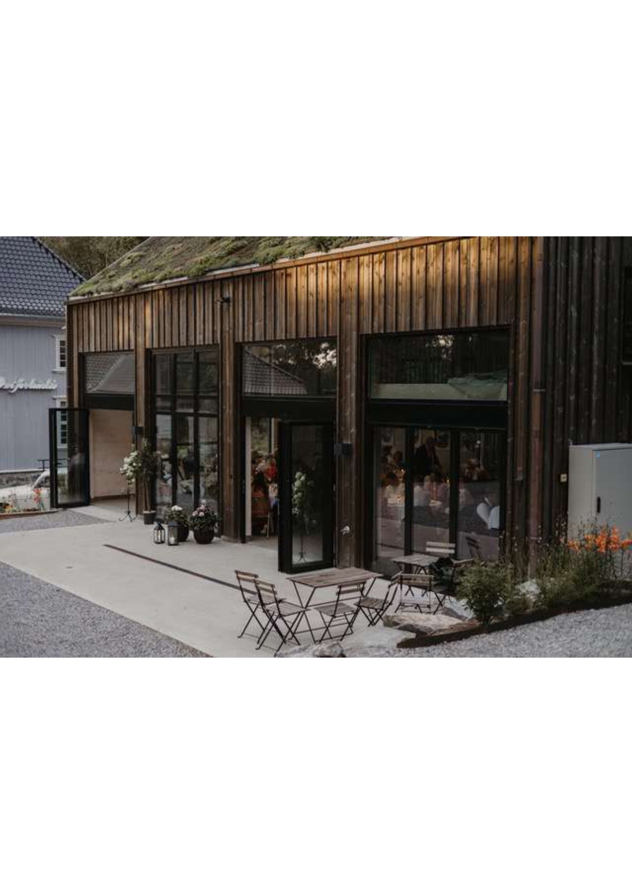 hus med stoler og bord utenfor med gjester inne i huset med store vinduer