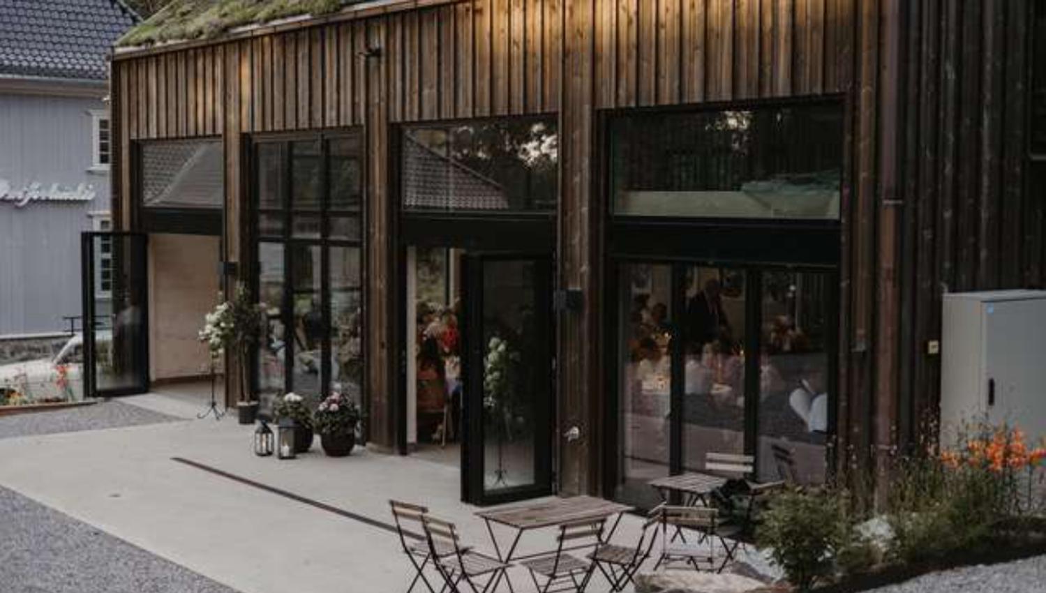 hus med stoler og bord utenfor med gjester inne i huset med store vinduer