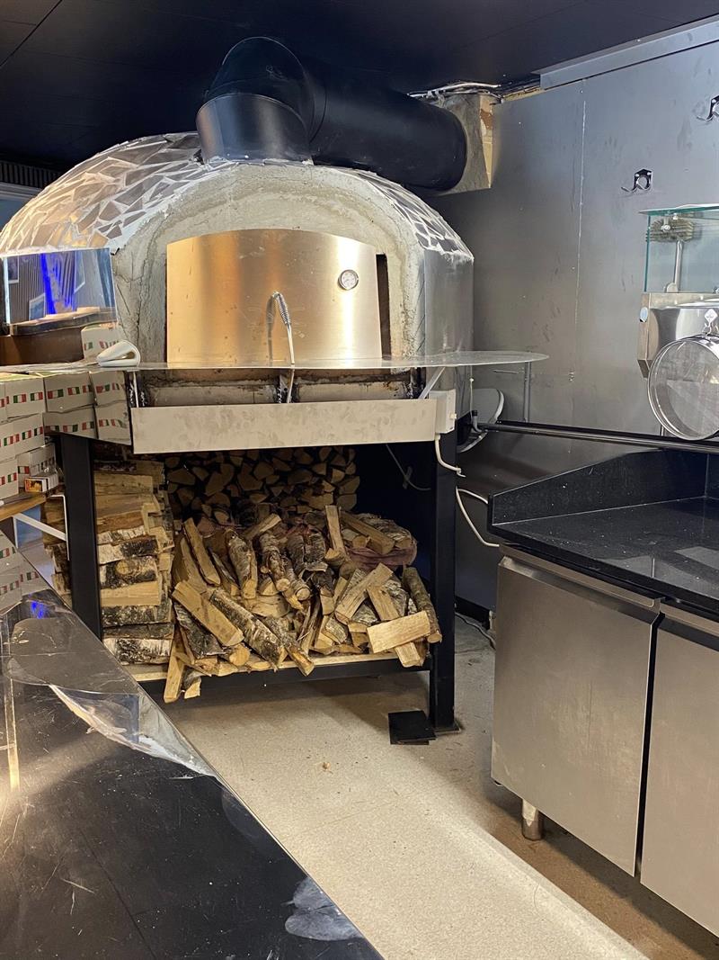 Bildet viser en steinovn med en stor vedstabel under for å bake pizza og calzone